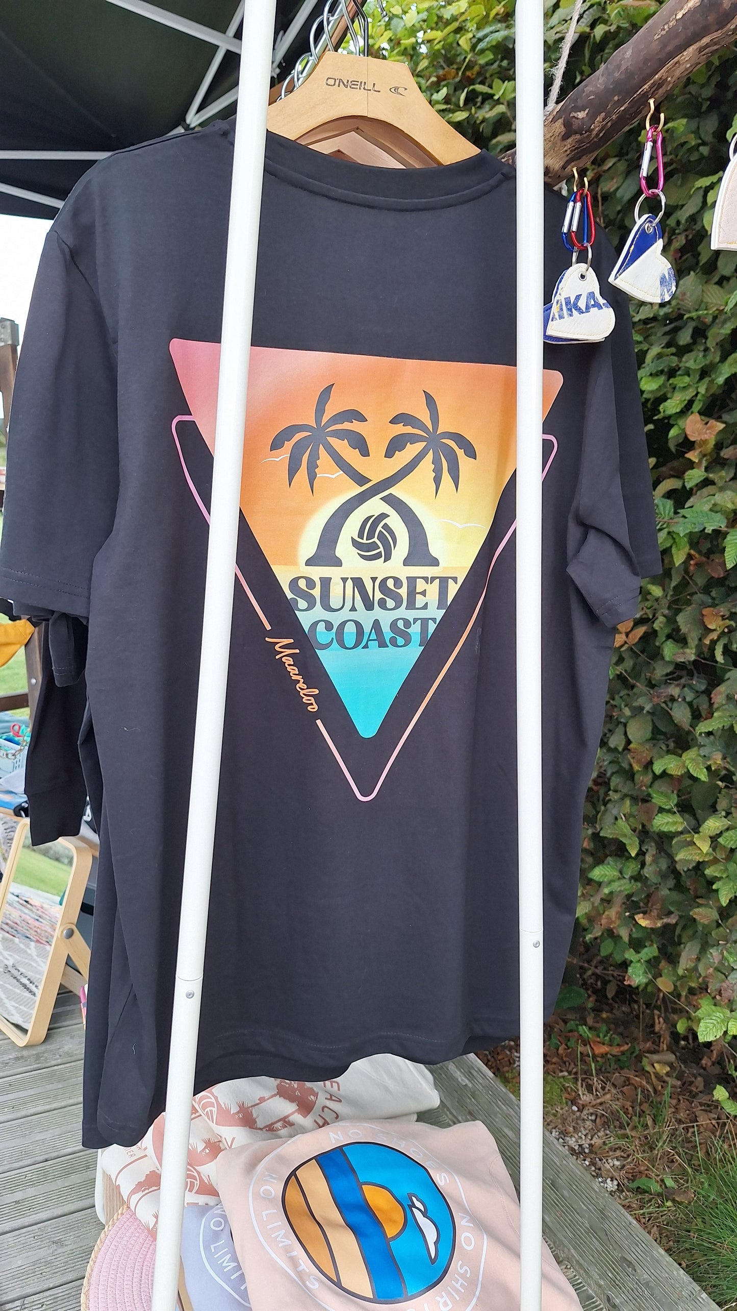 Beachvolleyball Bekleidung Streetwear Sportswear Oberteil Tshirt black mit Markenlabel Großer Rückenprint Sonnenuntergang im Dreieck Palmen Sunset Coast hängend an Kleiderstange